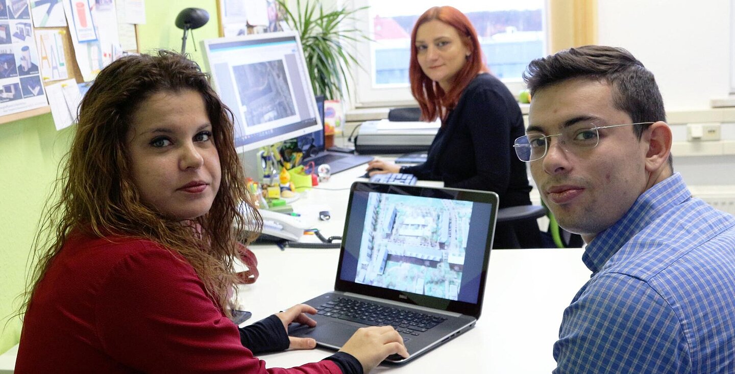 Meeting im Büro von Prof. Monica Rossi (Foto: Lena Ulrich) Aufnahme aus dem Büro der Professorin. Im Vordergrund sitzen die italienischen Doktoranden um einen Laptop herum, im Hintergrund sitzt Prof. Rossi an ihrem stationären Rechner. Beide Monitore zeigen Illustrationen einer Häuserzeile.