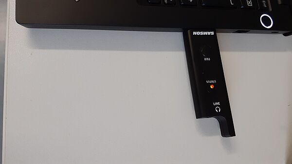 Ein schwarzer USB-Stick, der am PC angeschlossen den Verbindungsstatus zum Mikrofon anzeigt.