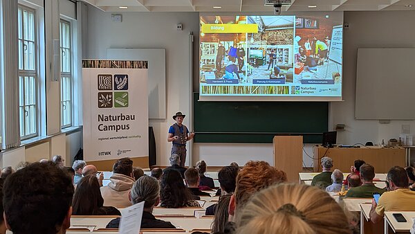 Eröffnung der Fachtagung. Hörsaal mit vielen Menschen, eine Person hält Vortrag vorn