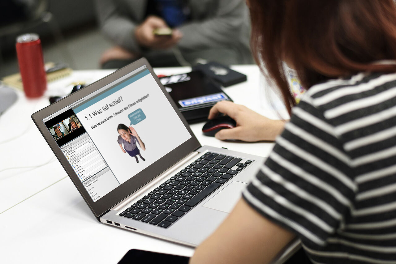 Eine studierende Person sitzt mit anderen Studierenden am Tisch und benutzt dabei einen Laptop.