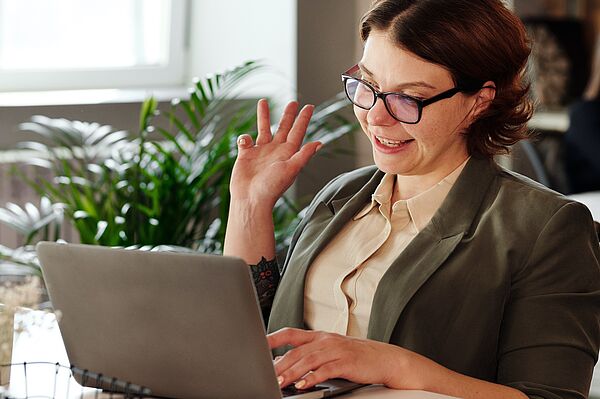 Frau sitzt in Businesskleidung vor dem Laptop und verfolgt eine digitale Veranstaltung