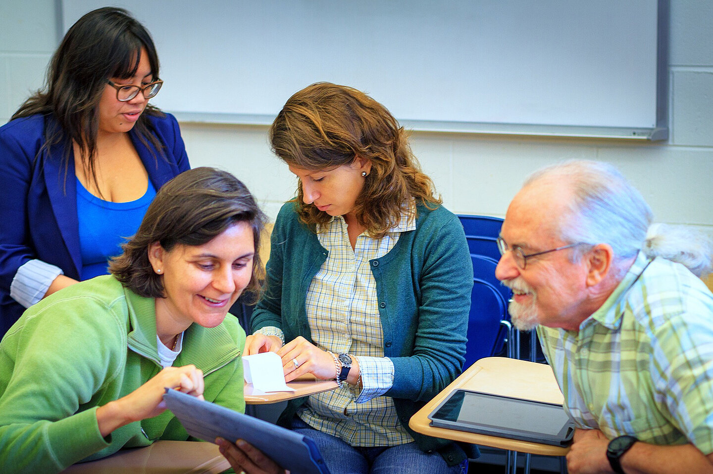 Foto von 4 Personen, die sich unterhalten und sich was auf dem Tablet zeigen.
