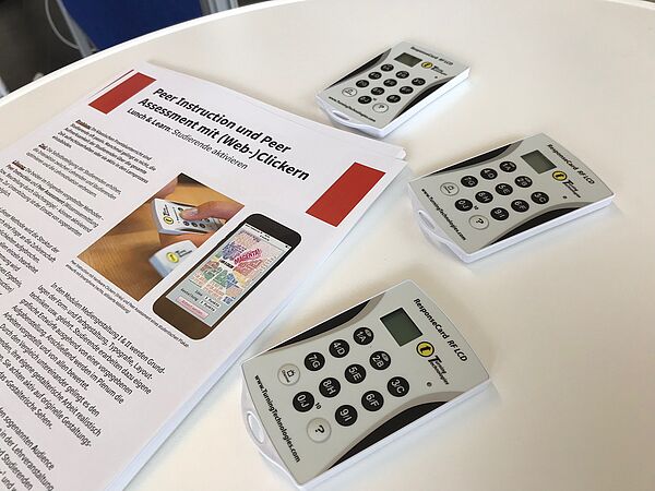 Drei digitale Abstimmungsgeräte (optisch ähnlich Taschenrechnern) und Benutzungshinweise auf einem Tisch.