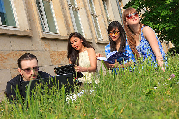 Drei Personen im Gras, z.T. mit Laptop.